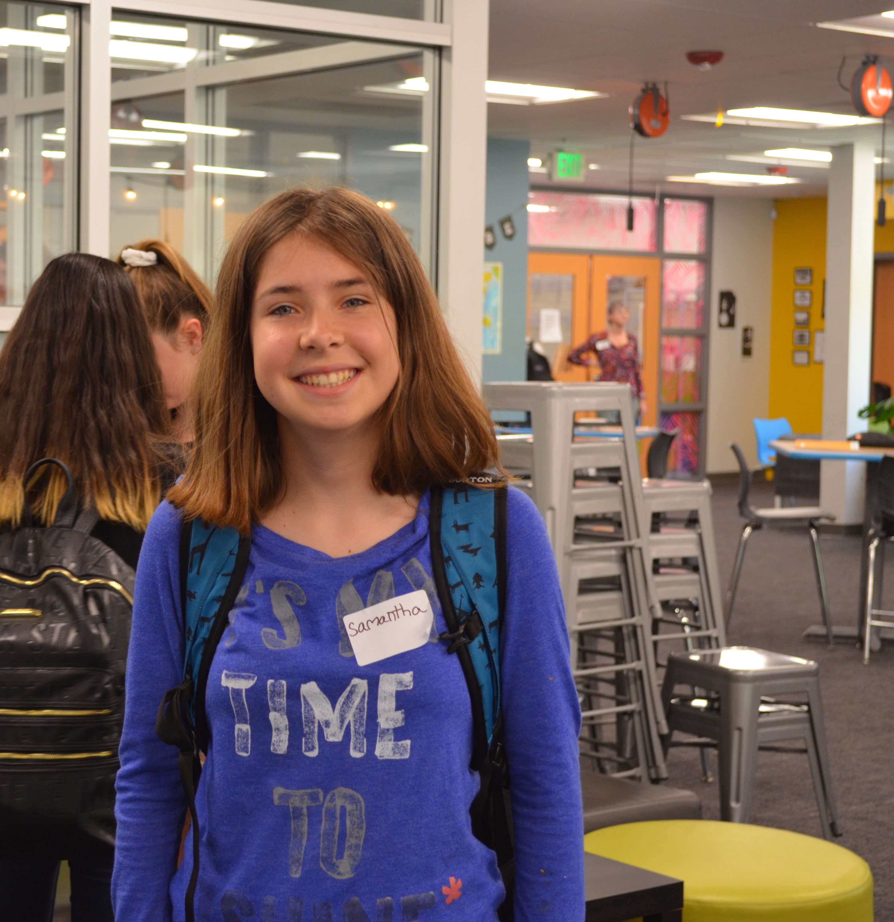 A student smiles for the camera while wearing a blue sweatshirt that reads "It's My Time to Shine."