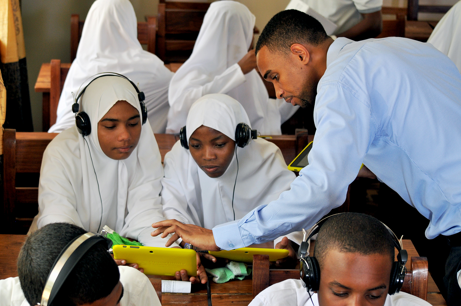 A Zanzibar classroom of students using Opportunity Tablets, provided by Opportunity Education, while a teacher works with two students, tapping the screen of their tablet.