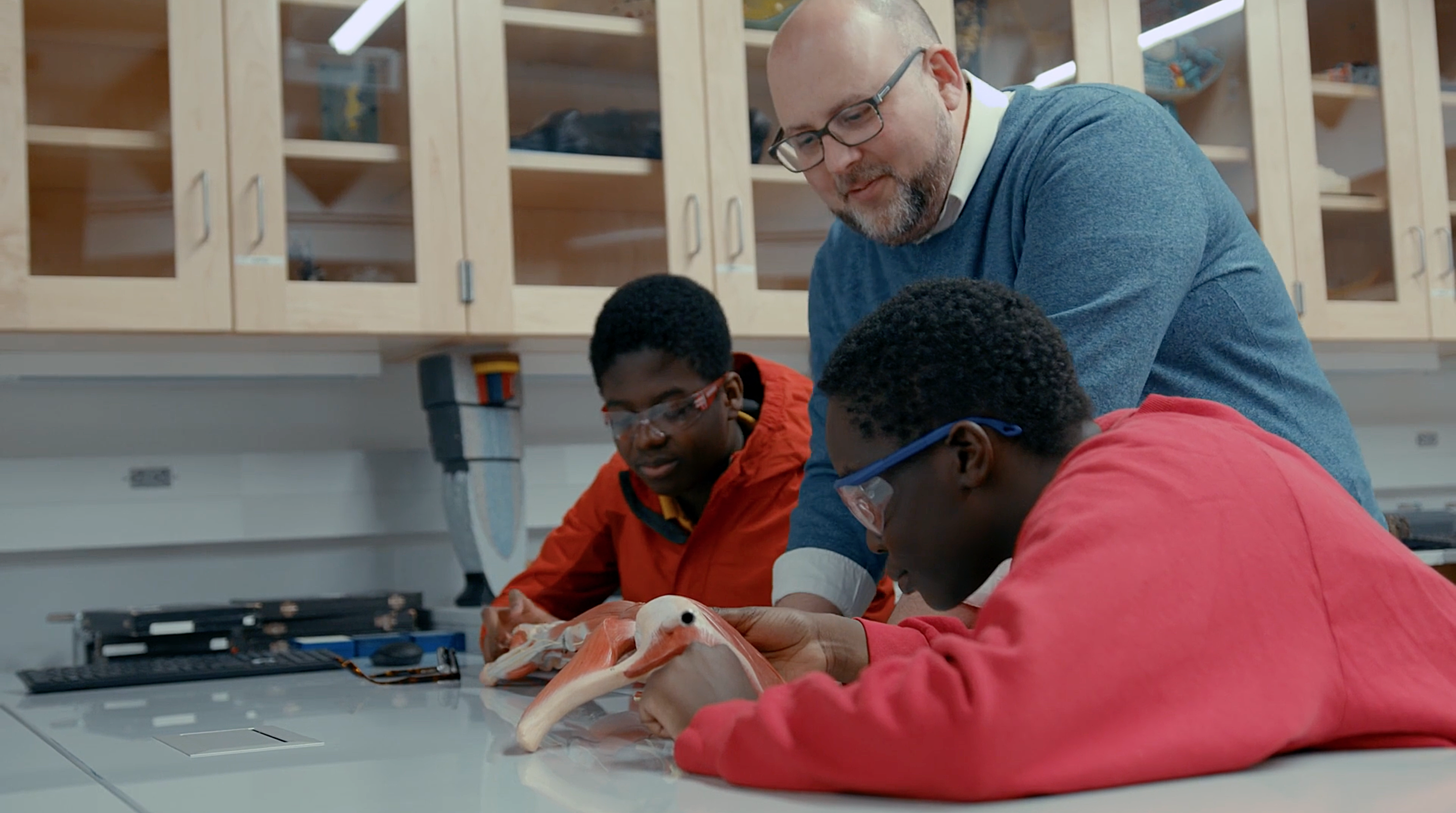 Two students study models of the human heart with Mark Smith, Director of Quest Forward Academy Omaha.