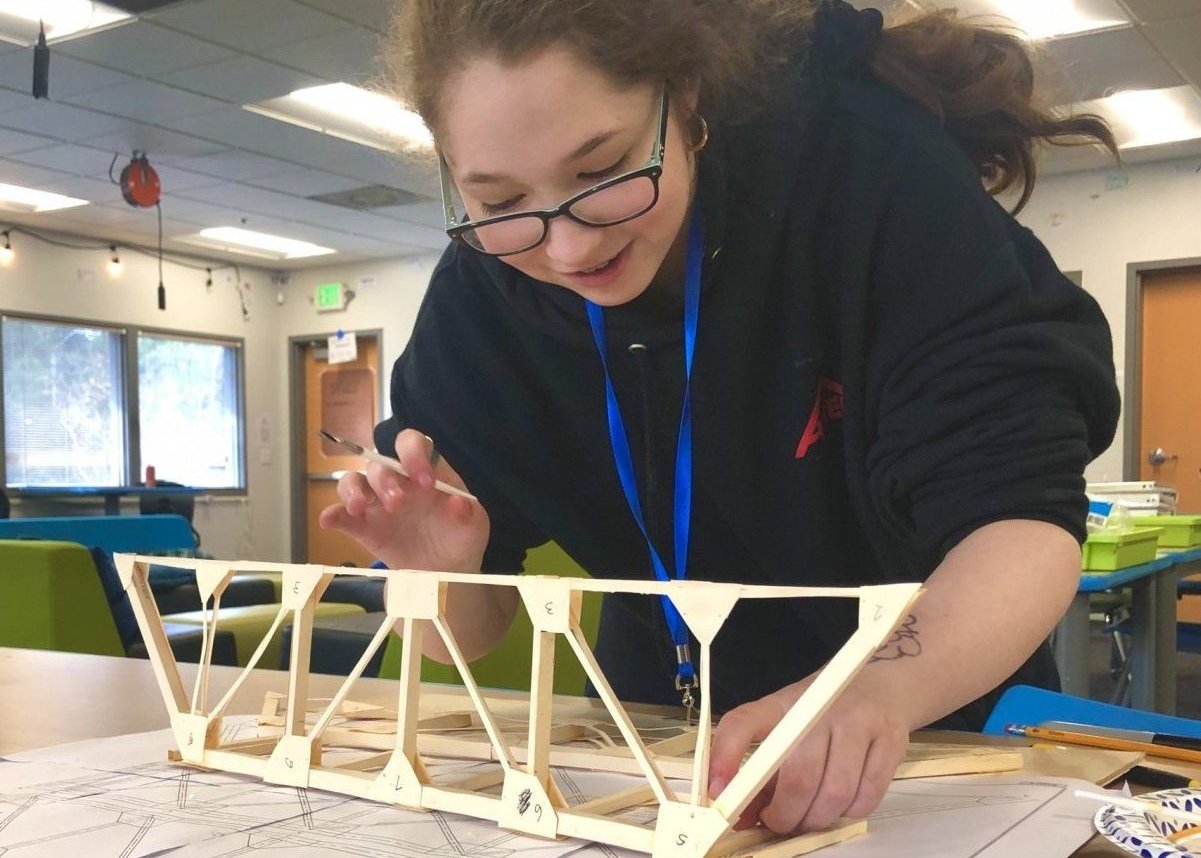 A smiling student examines a truss she built for a bridge-building project at Quest Forward Academy Santa Rosa.