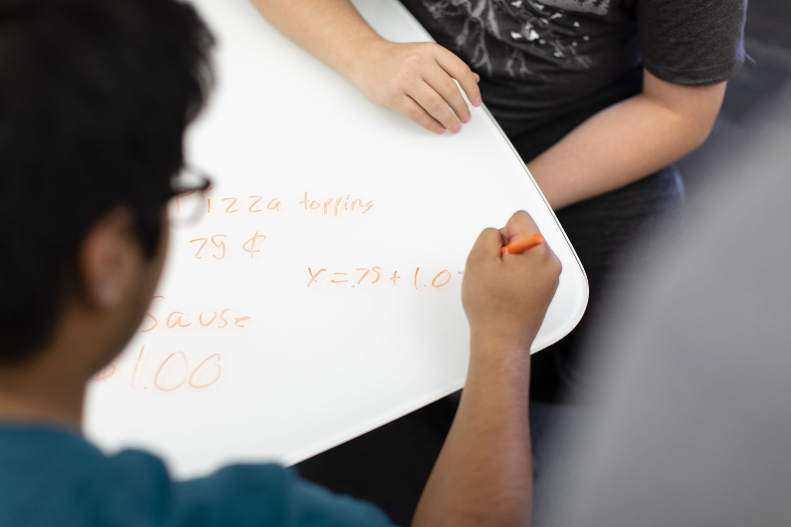 Two students work on a dry-erase tabletop, solving math equations, at Quest Forward Academy Omaha.