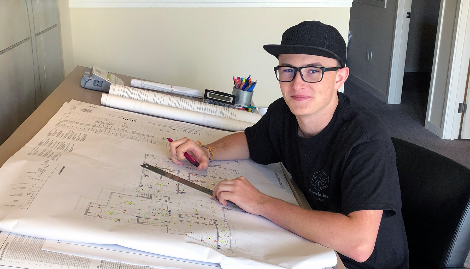 Pathways Program participant Graysen sits at his internship desk reviewing a building's electrical plans.