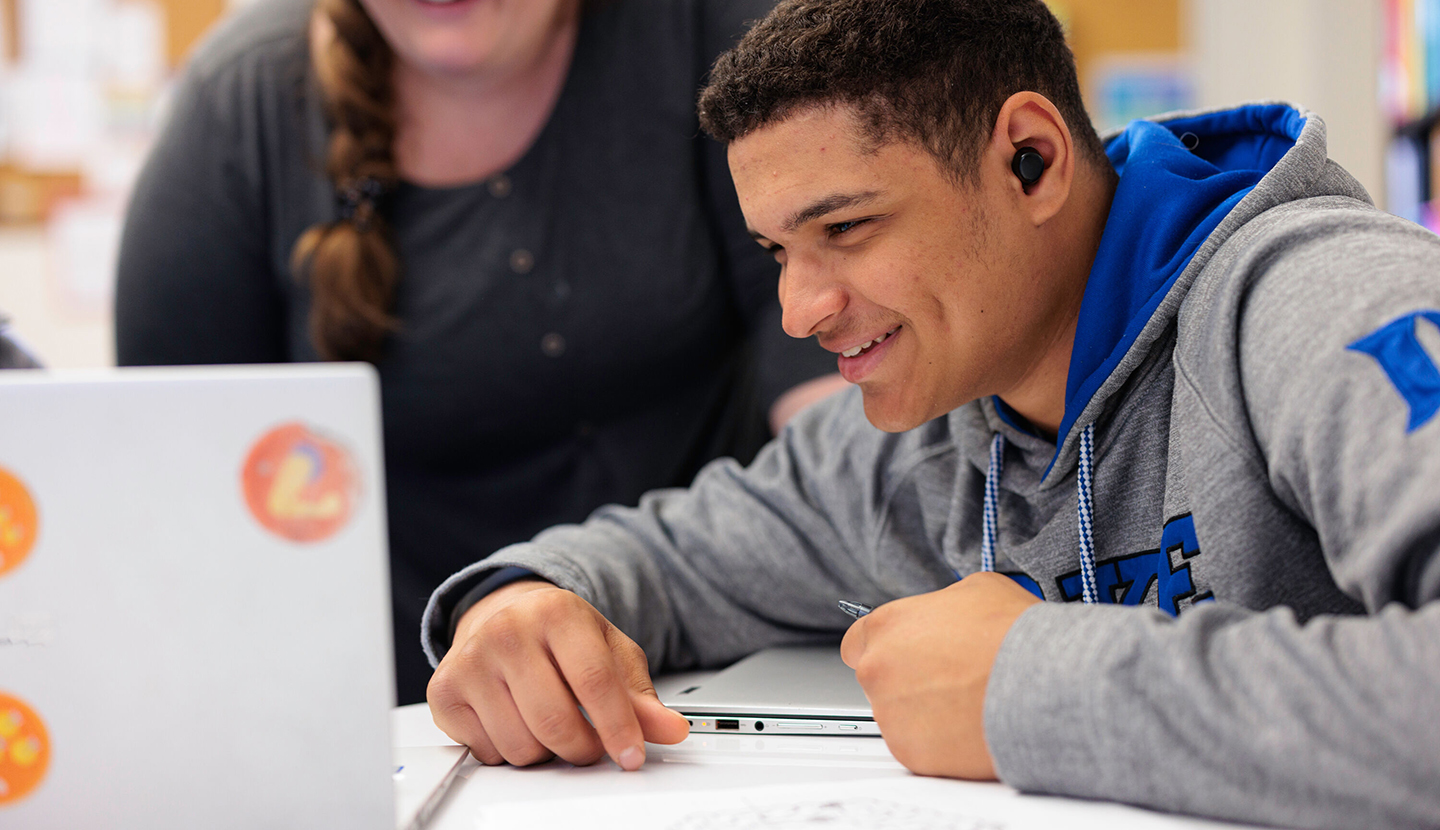 A student at Quest Forward Academy Omaha smiles brightly as he looks at the Quest Forward LMS on his laptop