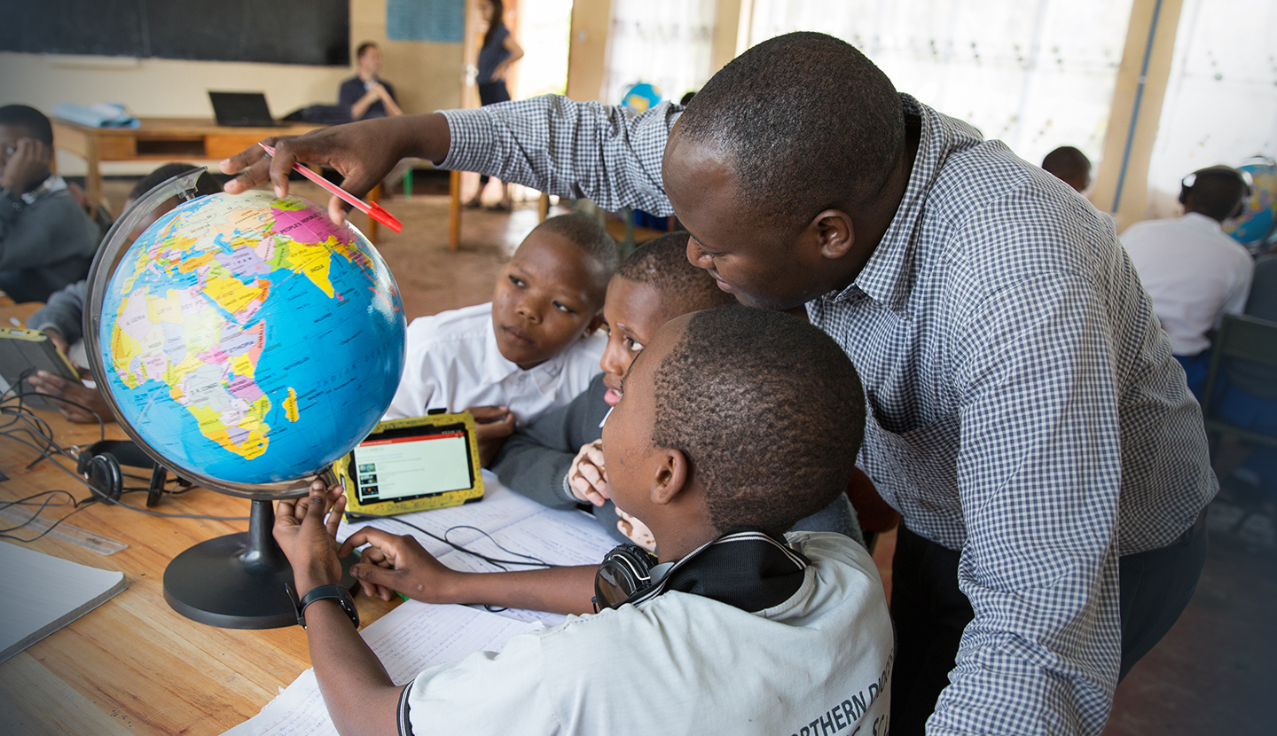 A teacher at Mtakuja Secondary School in Tanzania gestures to points on a globe while working with his students.