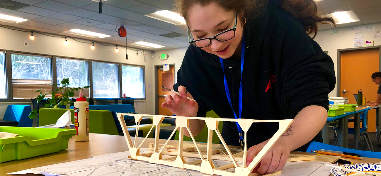 A smiling student at Quest Forward Academy Santa Rosa builds a paper bridge from blueprints.
